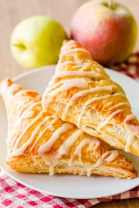 two apple turnovers on a plate with glaze