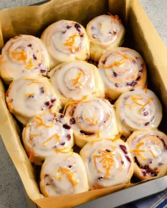 12 baked cranberry cinnamon rolls with orange glaze parchment lined baking dish.