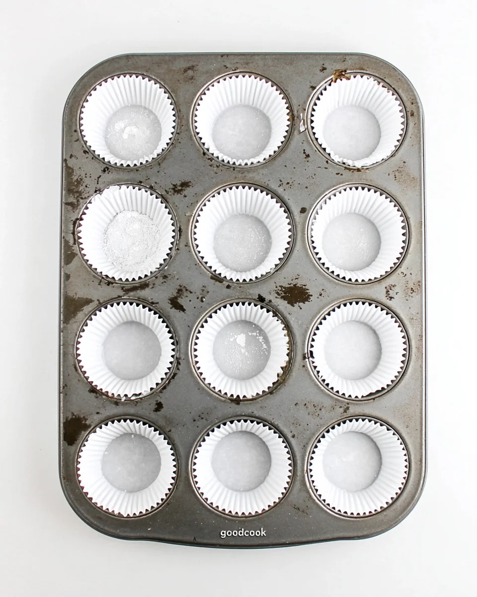 Metal muffin pan lined with white paper cupcake liners, ready for batter to be poured. Metal muffin pan lined with white paper cupcake liners, ready for batter to be poured.
