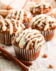 Close-up of golden-brown pumpkin spice muffins with creamy white cream cheese frosting melting slightly on top.