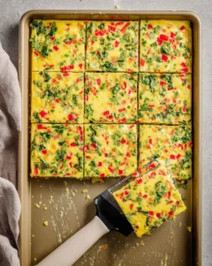 baked sheet pan omelette with spinach and bell peppers sliced into squares with spatula taking out one serving.