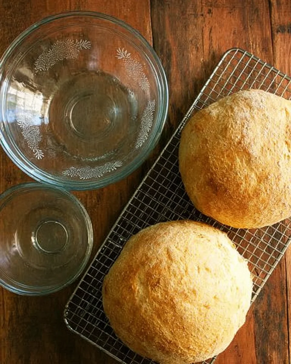 Two fresh loaves of peasant bread, two glass pyrex bowls, and cooling rack