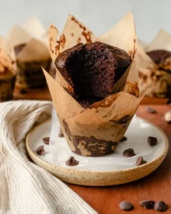 two chocolate protein muffins in parchment muffin liners stacked on each other.