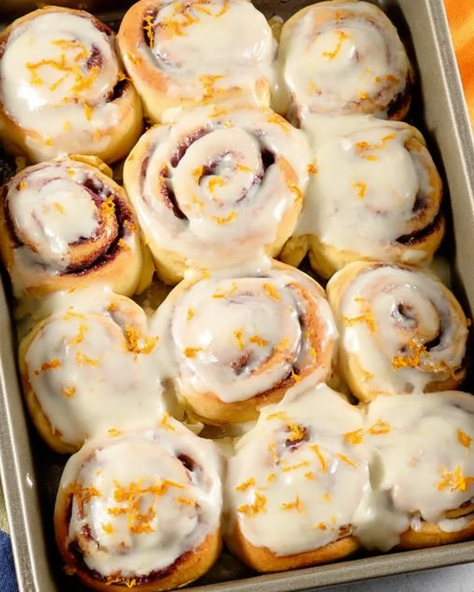 12 baked cranberry cinnamon rolls with orange glaze parchment lined baking dish.