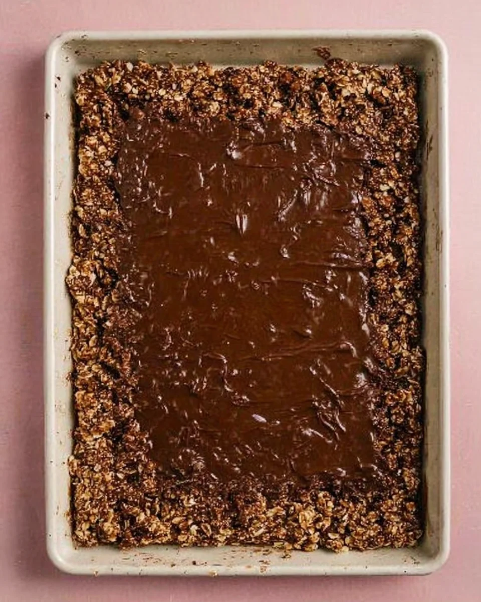 chocolate peanut butter granola on white sheet pan spread with melted chocolate.