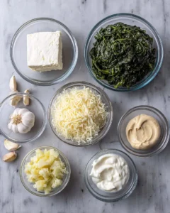 The image shows seven clear glass bowls of different sizes placed on a white marbled surface. Starting from the top left, the first bowl contains a solid block of white cream cheese. Next to it, a bigger bowl is filled with dark green, slightly frosty spinach. To the right, another large bowl holds a heap of shredded white mozzarella cheese. Below the top row, from left to right, there is a small bowl with chopped pale yellow artichoke pieces, a smaller bowl with grated pale yellow Parmesan cheese, a medium bowl filled with thick white sour cream, and a small bowl with a dollop of smooth beige mayonnaise. Three pieces of garlic cloves sit beside the bowls on the left. The photo is taken with an iPhone --ar 4:5 --v 7