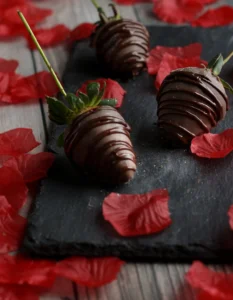 Chocolate covered strawberries on a slate plate surrounded by rose petals for a delicious treat to enjoy on date night, or a Tuesday.
