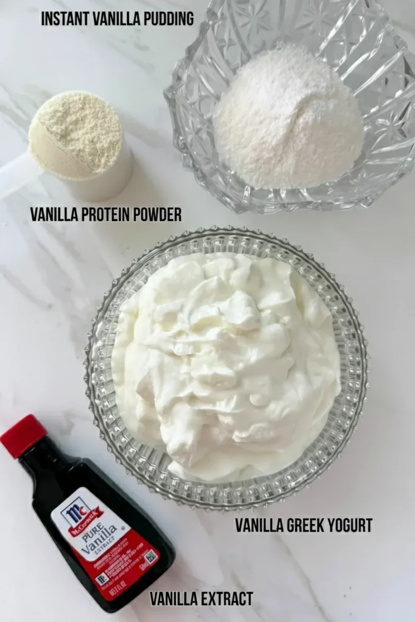 High-Protein-Vanilla-Pudding-Ingredients-683x1024.webp Collection of vanilla ingredients including Greek yogurt, vanilla pudding, protein powder, and vanilla extract on a white background.
