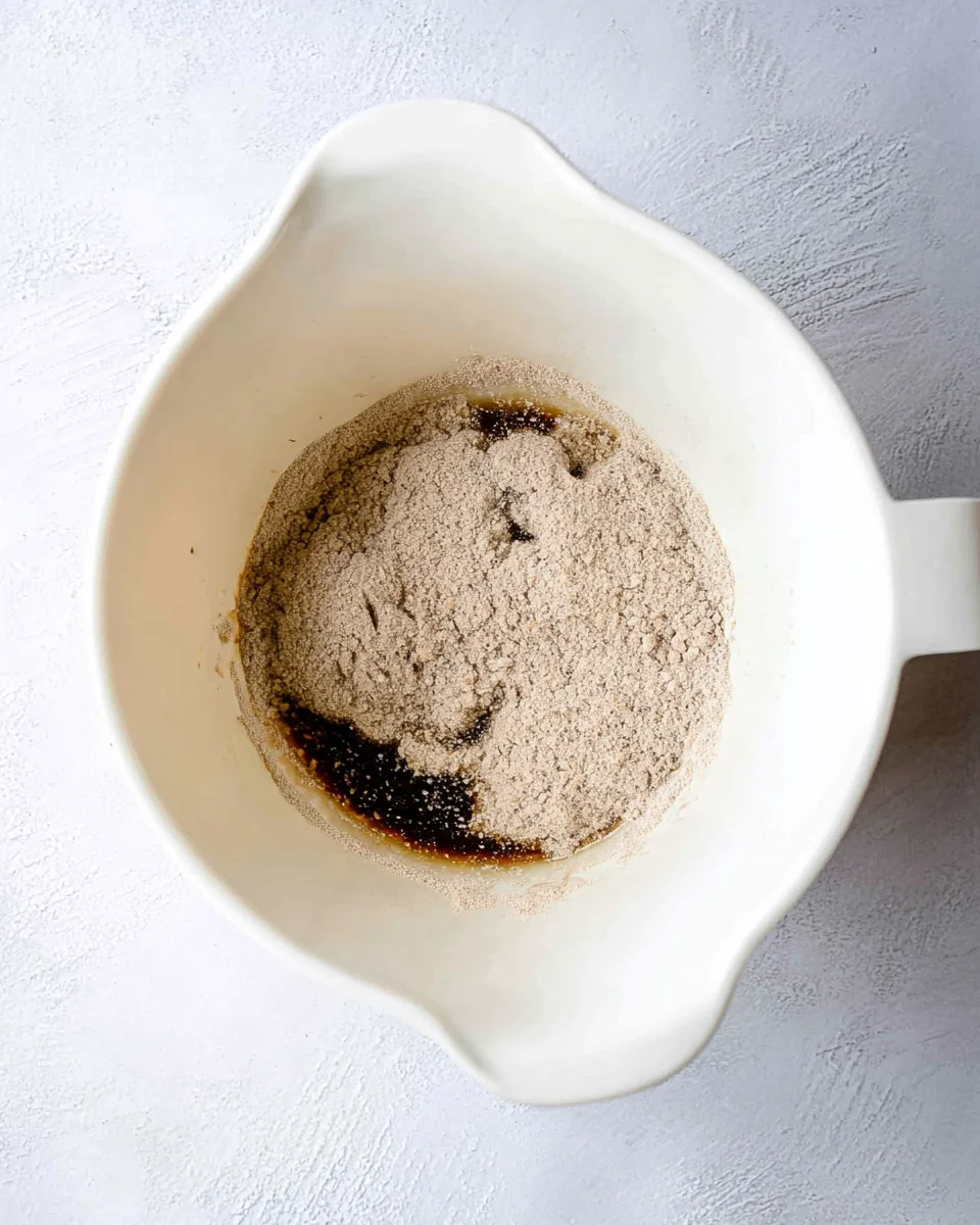 Wet and dry ingredients for outback bread in a white mixing bowl. 