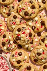 Peppermint chip cookies arranged on surface with chopped candy canes in bowl.