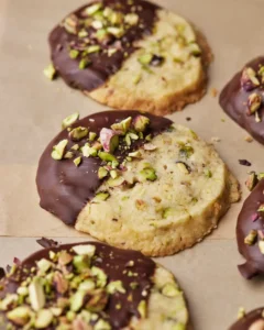 Round pistachio shortbread cookies in a row, dipped in chocolate and topped with chopped pistachios.