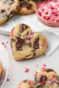heart shaped cookie leaning against white parchment paper with cookies and sprinkles in the background