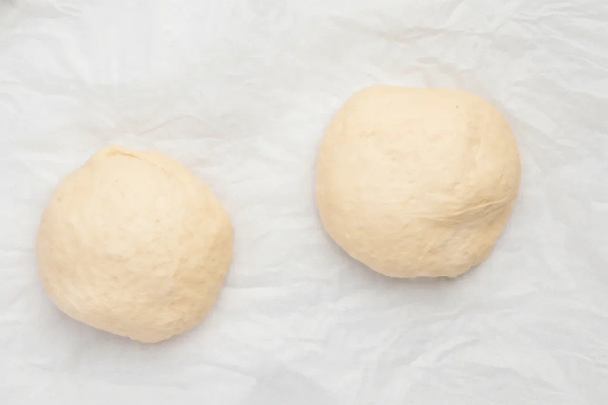 Two round balls of dough on a white surface, ready for baking or cooking.