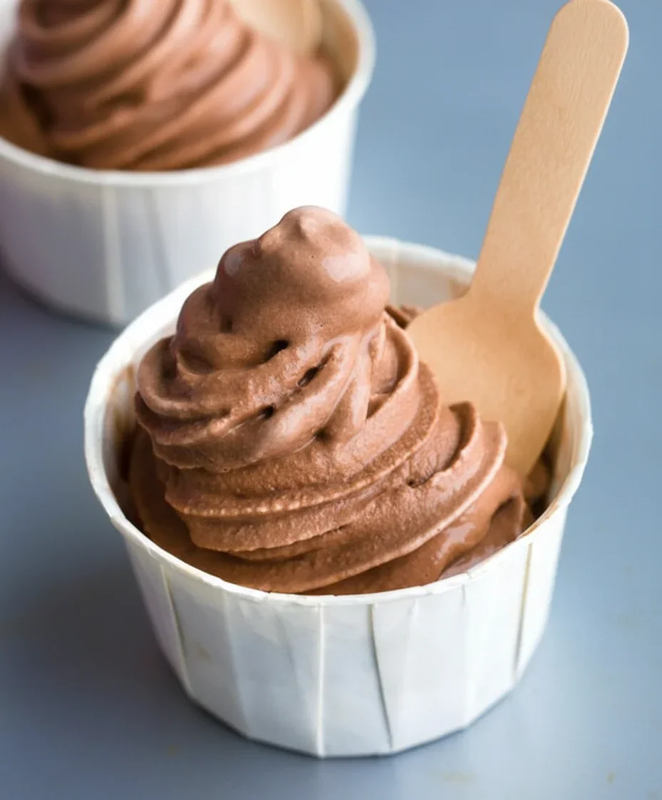 Close-up of a white cup filled with swirled chocolate ice cream and a wooden spoon.