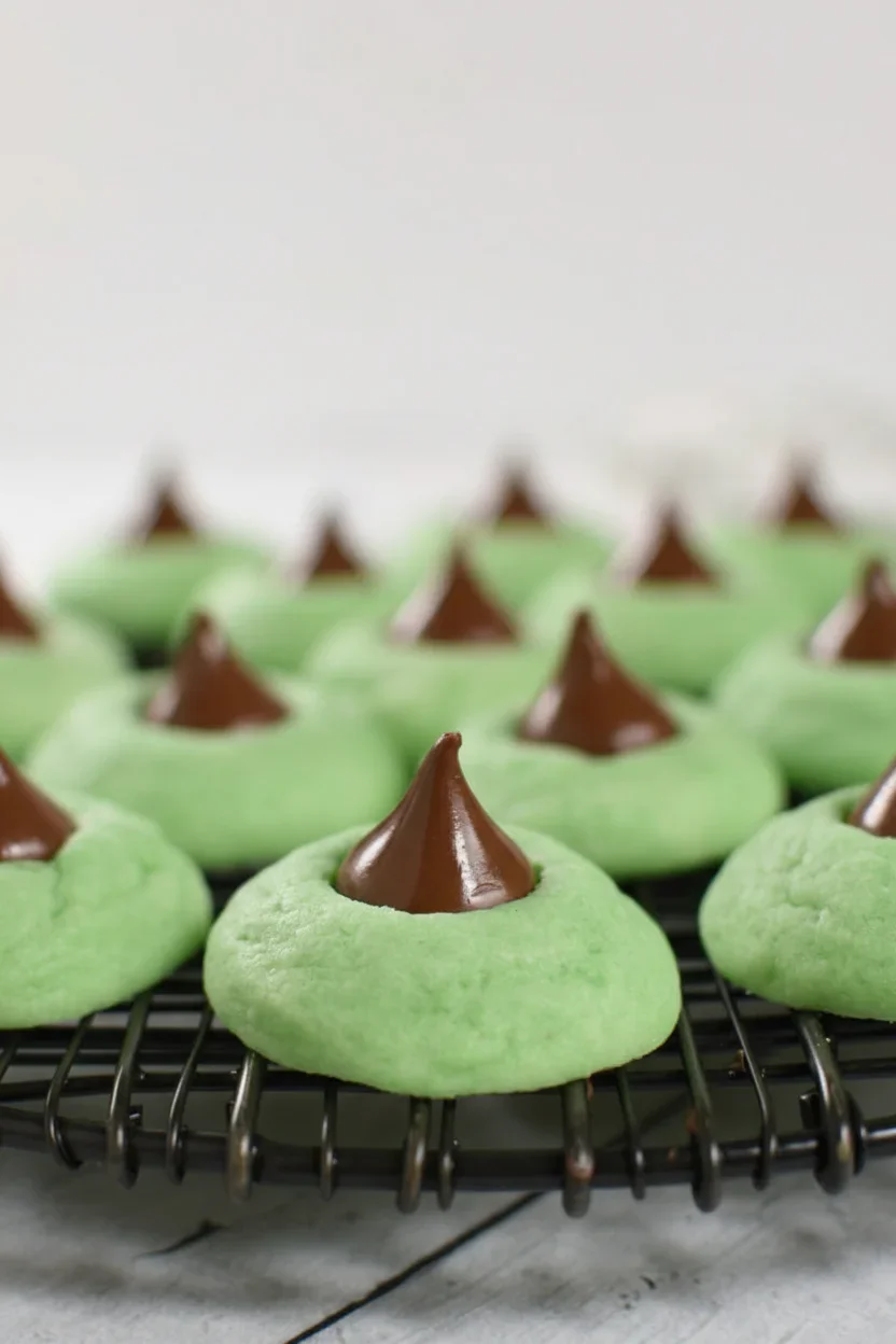 Bright green cookies with melted chocolate peaks on a black cooling rack, on a light gray background.