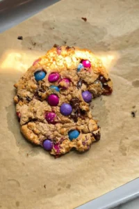 oatmeal protein cookie with m&ms and chocolate chips on a baking sheet with a bite taken out