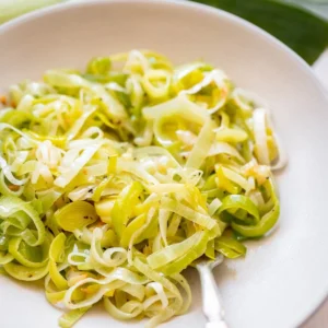 A silver fork rests in a large ceramic bowl of cooked, sliced green leeks.