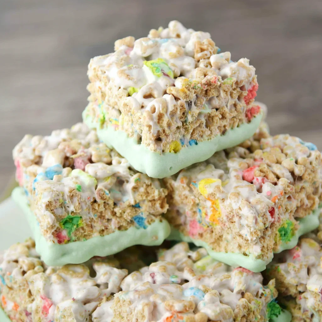 Stack of colorful rice cereal treats with pastel coating and sprinkles, on a wooden background.