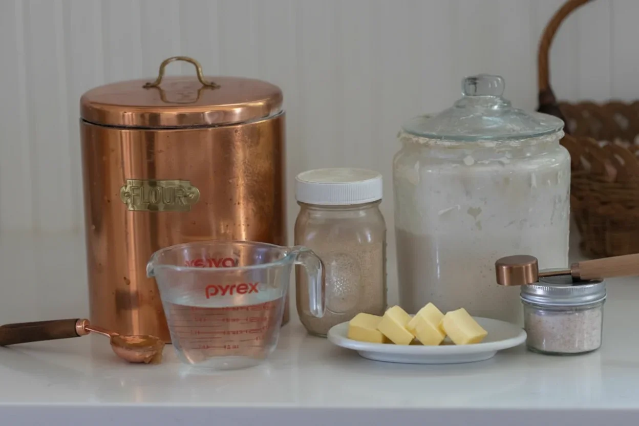 Collection of baking ingredients including flour, butter, sugar, and measuring tools on a white surface.