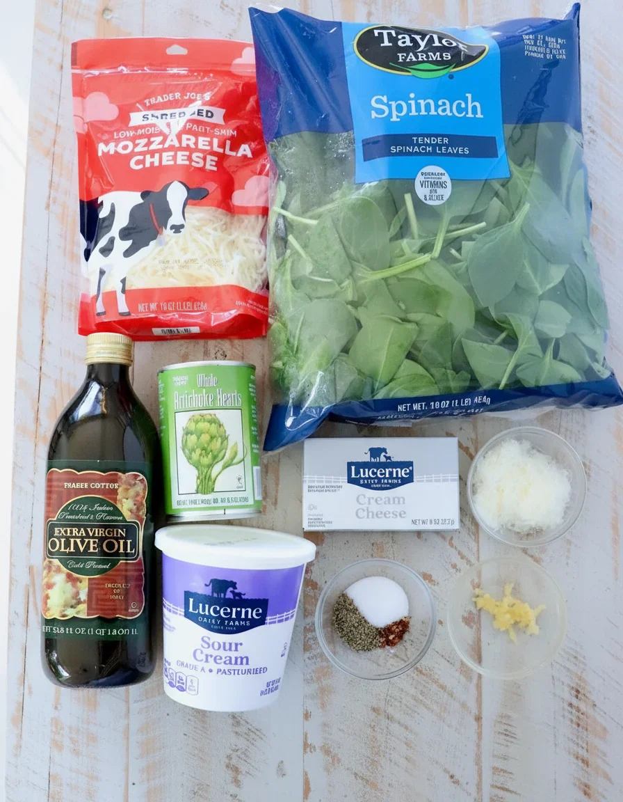 Assorted fresh ingredients including spinach, cheeses, olive oil, and seasonings arranged on a wooden surface.