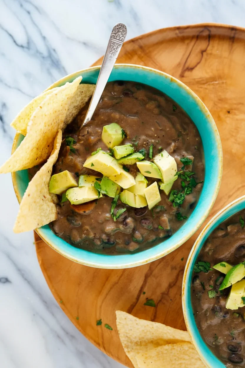vegetarianvegan-black-bean-soup-recipe-3.jpg A bowl of black bean soup topped with avocado chunks and cilantro, with tortilla chips on the side.