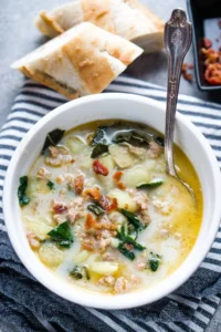 zuppa toscana soup in white bowl on striped linen with baguettes