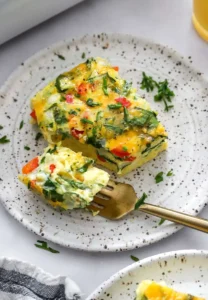 Slice of cottage cheese egg bake with veggies in it on a plate with a fork on the plate with it.