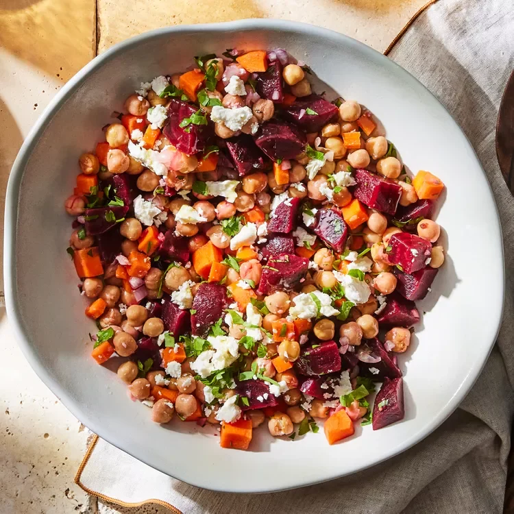 Colorful salad with chickpeas, beets, feta, and fresh herbs in a white bowl.