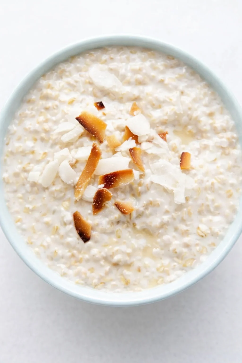 top-down view of a pale-blue bowl of creamy oatmeal topped with toasted coconut flakes