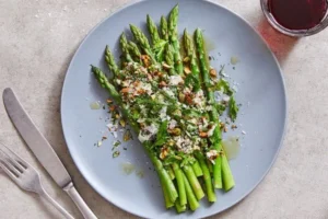 Fresh asparagus salad topped with shaved cheese and toasted pistachios on a plate.