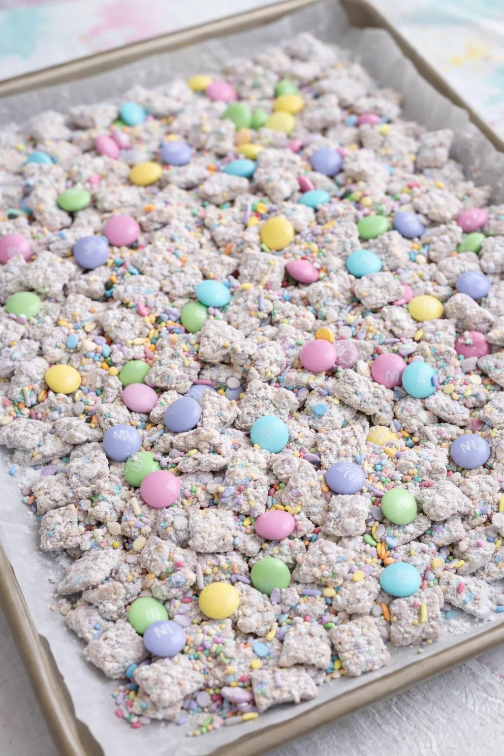 step-process-placeholder-5-8.png Powdered, chocolate-coated cereal spread on parchment with pastel M&Ms and sprinkles being stirred