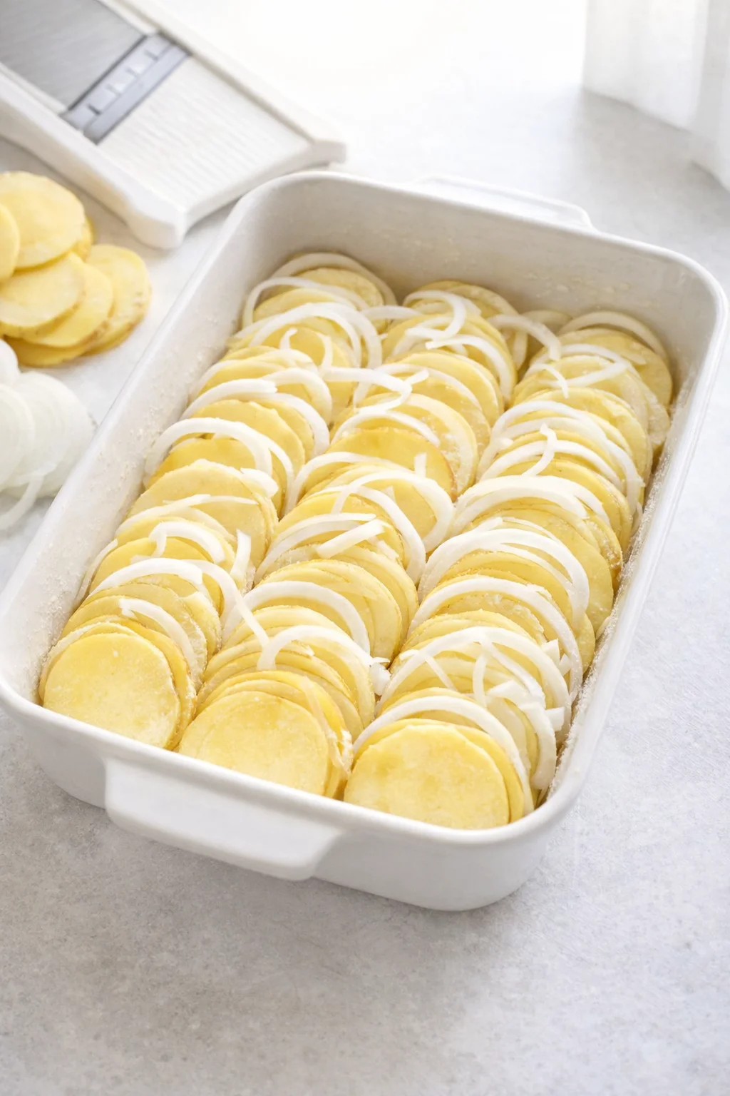 Neatly arranged slanted rows of thin potato slices and onion in greased casserole dish.