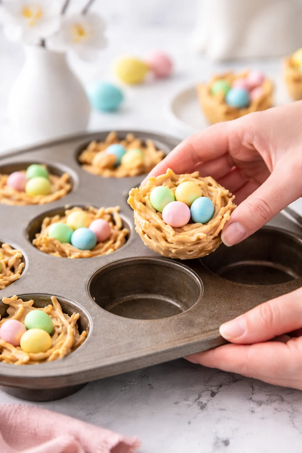 Hand flexing to pop a firm peanut-butter haystack from muffin tin, three eggs visible.