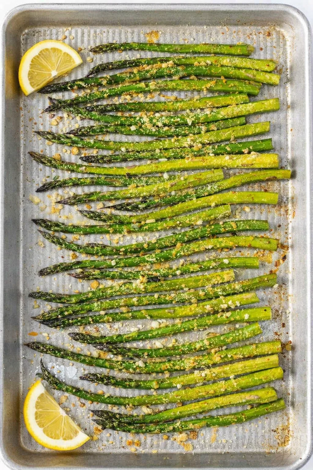 Roasted asparagus spears with slightly browned tips being sprinkled with grated Parmesan.
