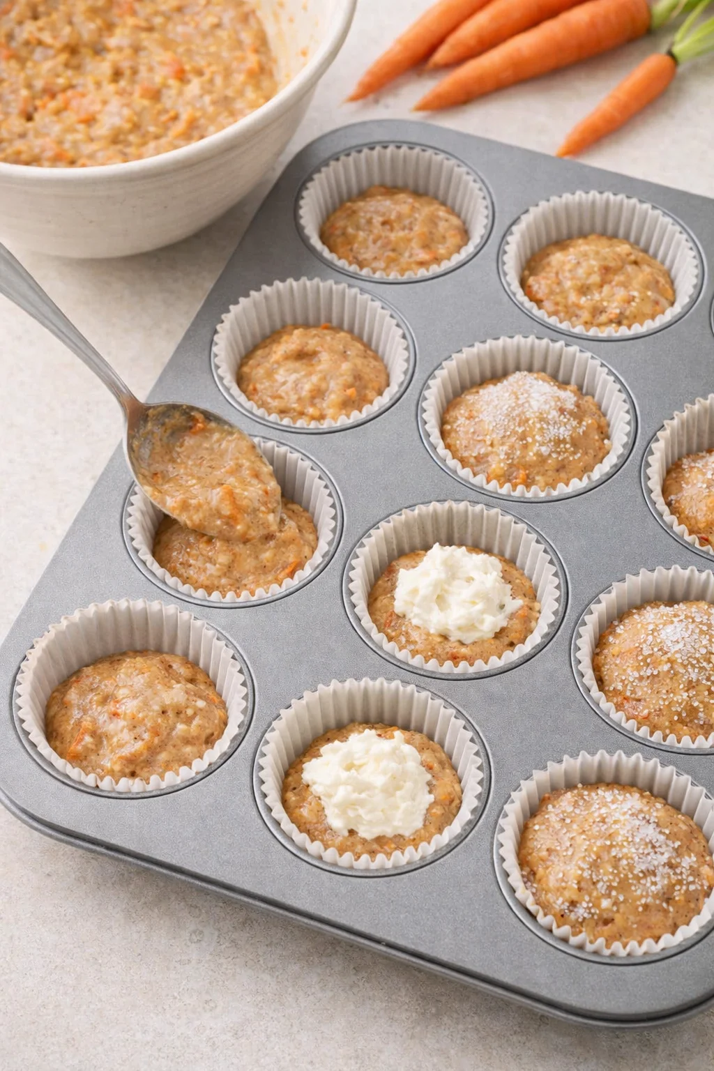 Muffin liners filled with batter, cream cheese dollops centered, tops sprinkled with sanding sugar.
