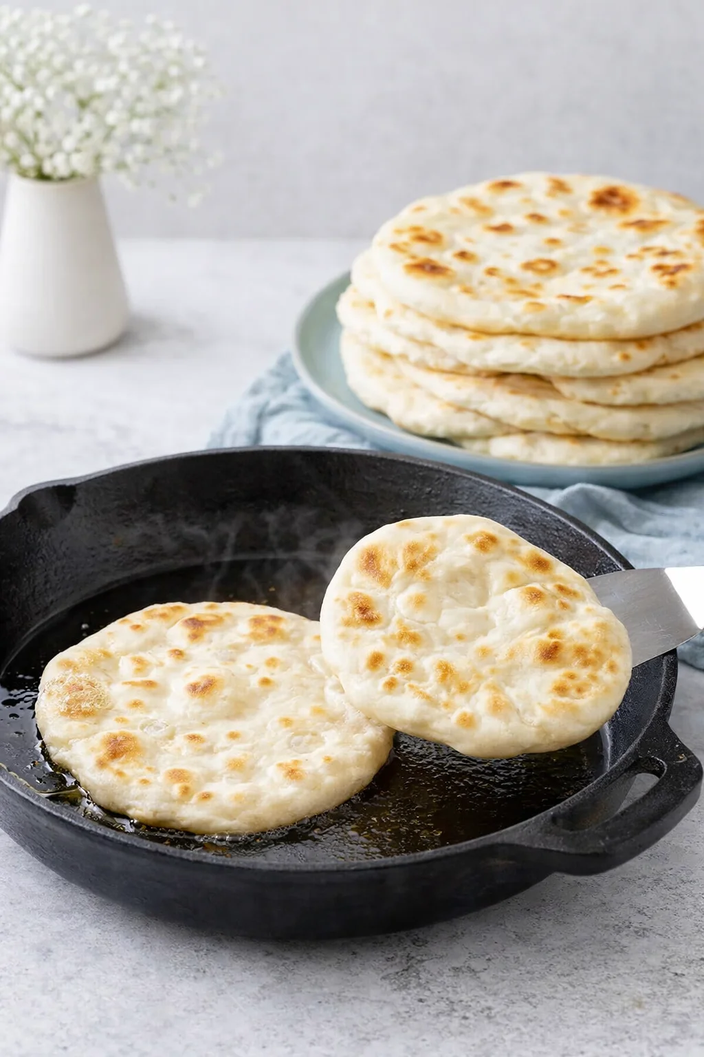 Pita circle sizzling in hot skillet, bubbling and puffing to light golden, ready to flip.