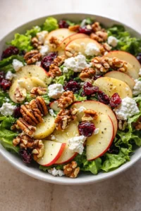 Vibrant salad with lettuce, apple slices, walnuts, dried cranberries, and crumbled cheese.