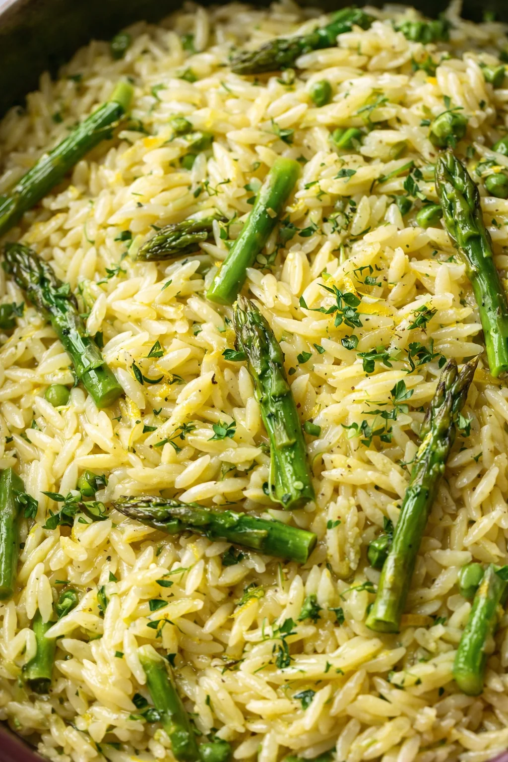 Creamy orzo with bright asparagus spears and fresh herbs in a pan.