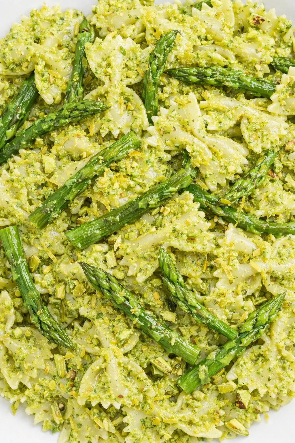 Bow-tie pasta with pistachio pesto and asparagus spears on a white plate