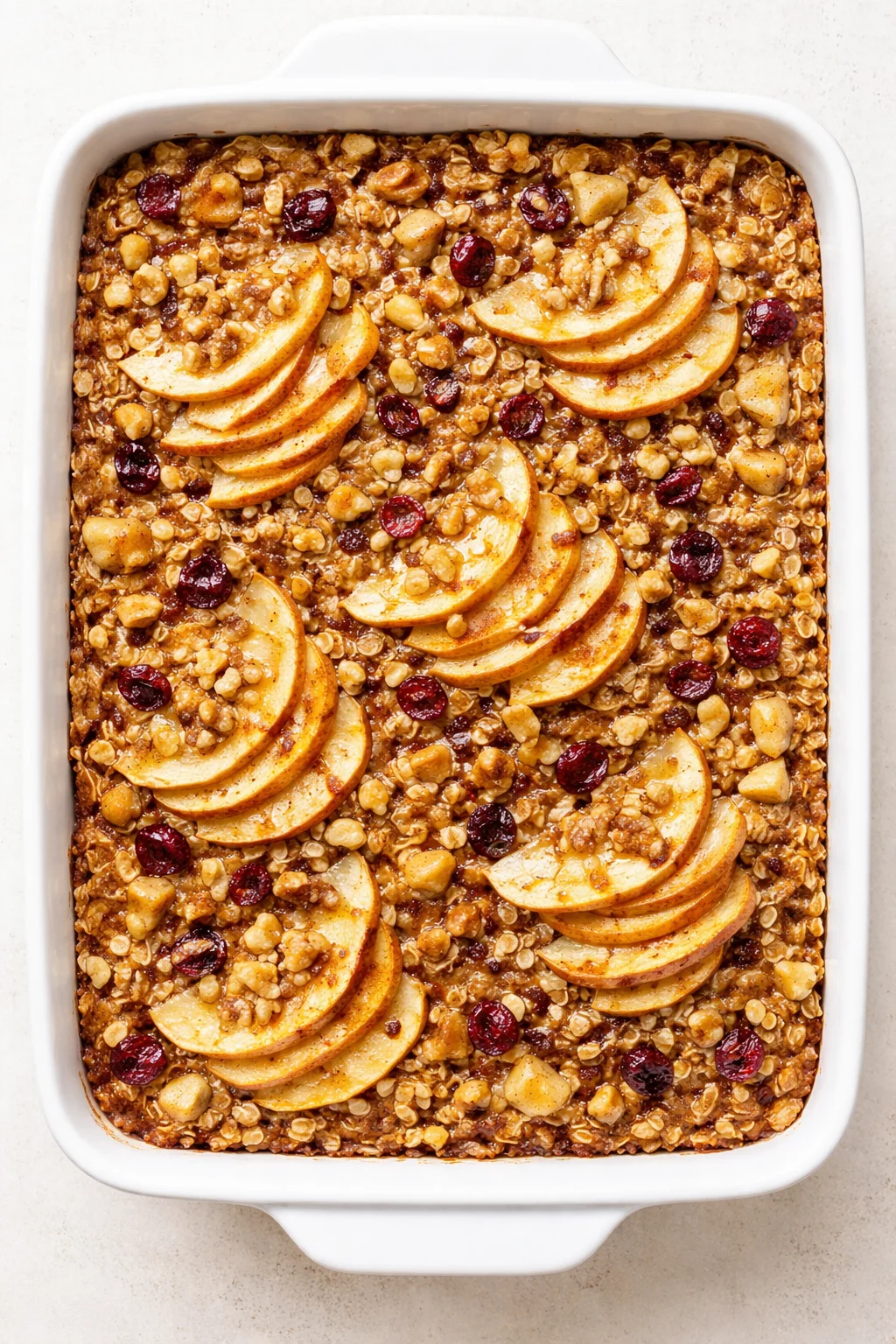 Overhead view of a white rectangular baking dish filled with baked apple crisp, topped with apple slices and oats.