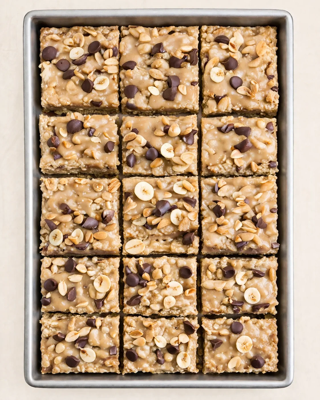 Top-down view of a pan of square caramel oat bars topped with banana chips, almonds, and chocolate chips