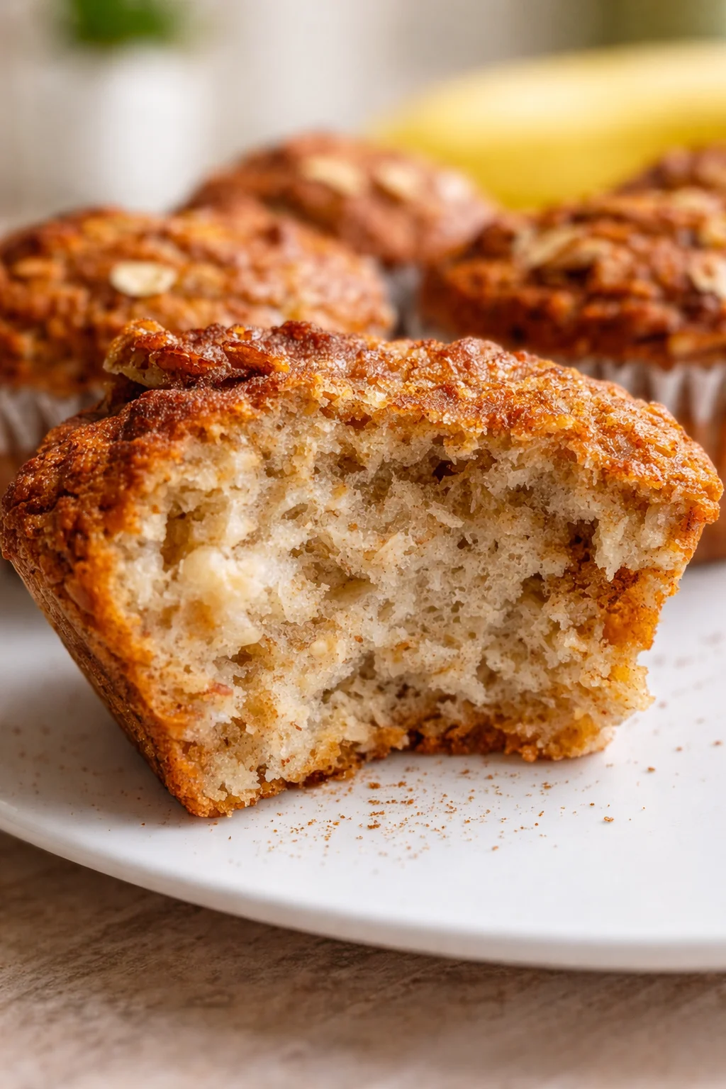 Close-up of a crumbly banana muffin on a white plate, golden crust visible