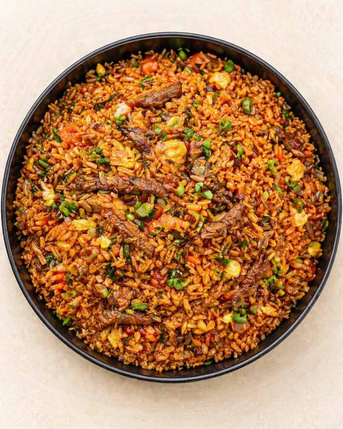 round black bowl of savory beef fried rice with vegetables and green onions on a light background