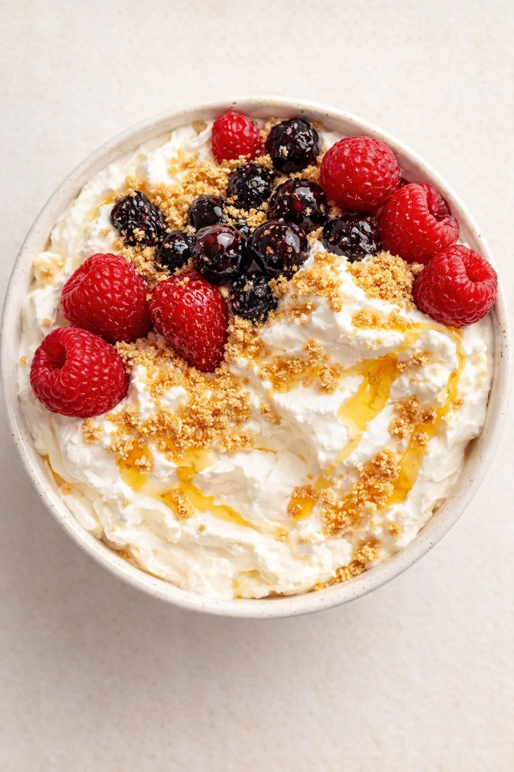 top-down view of a whipped-cream dessert bowl topped with raspberries, blueberries, and crumbs