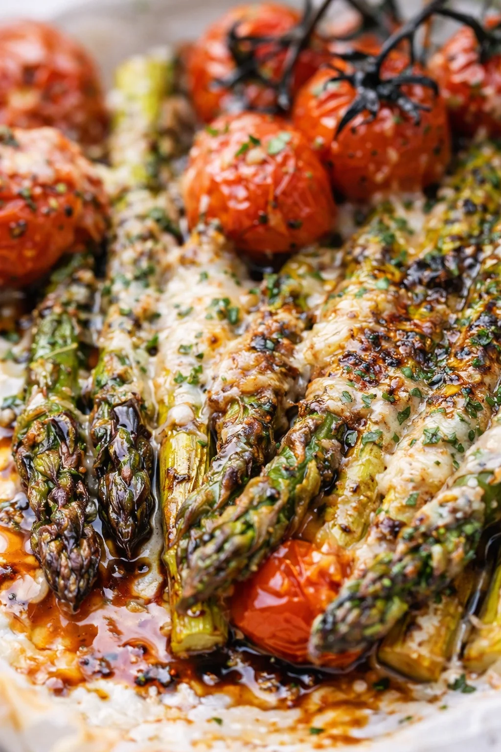 Close-up of roasted asparagus and cherry tomatoes with melted cheese and herbs.