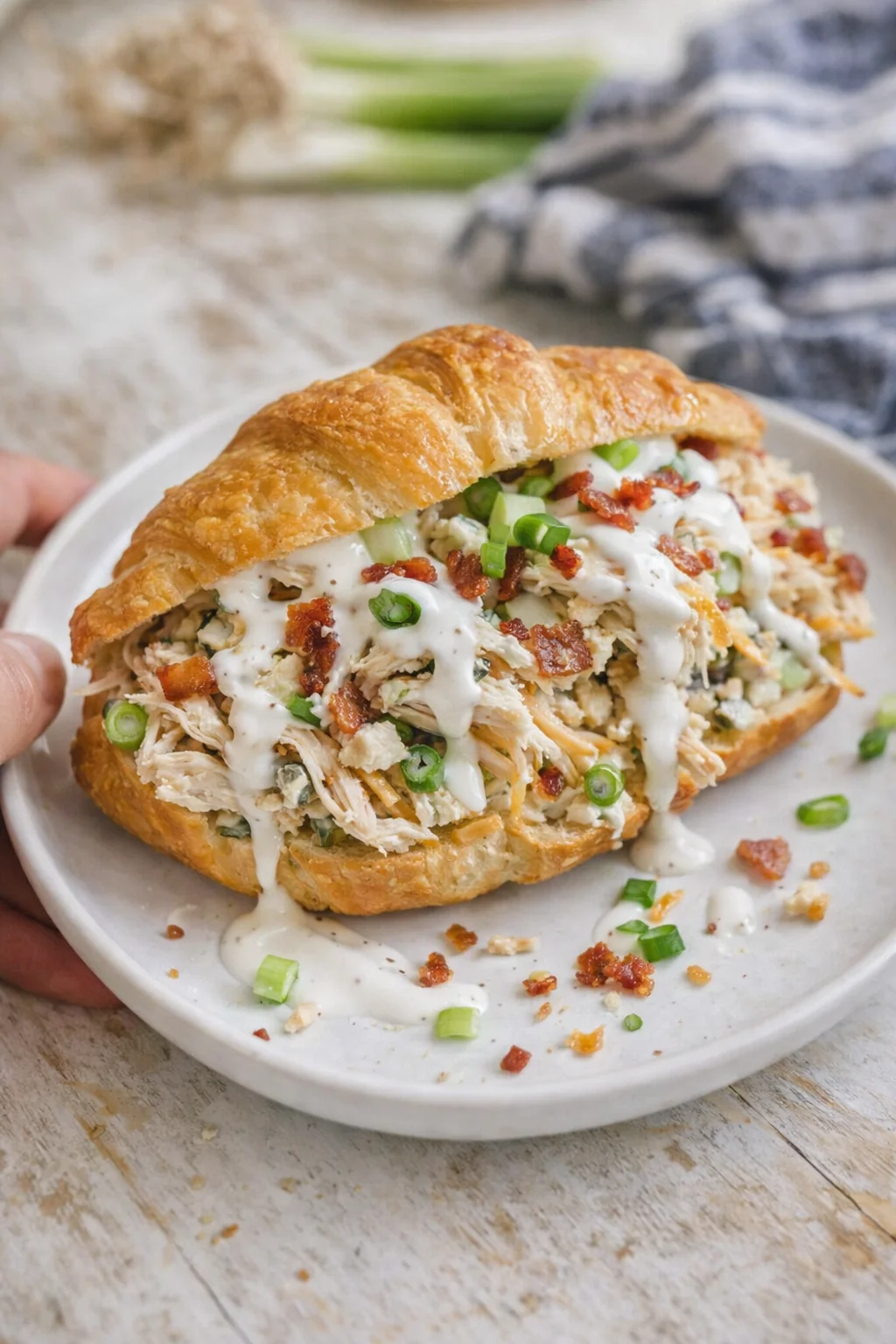 Golden croissant sandwich filled with creamy chicken salad, bacon bits, chopped green onions, drizzled with white sauce.