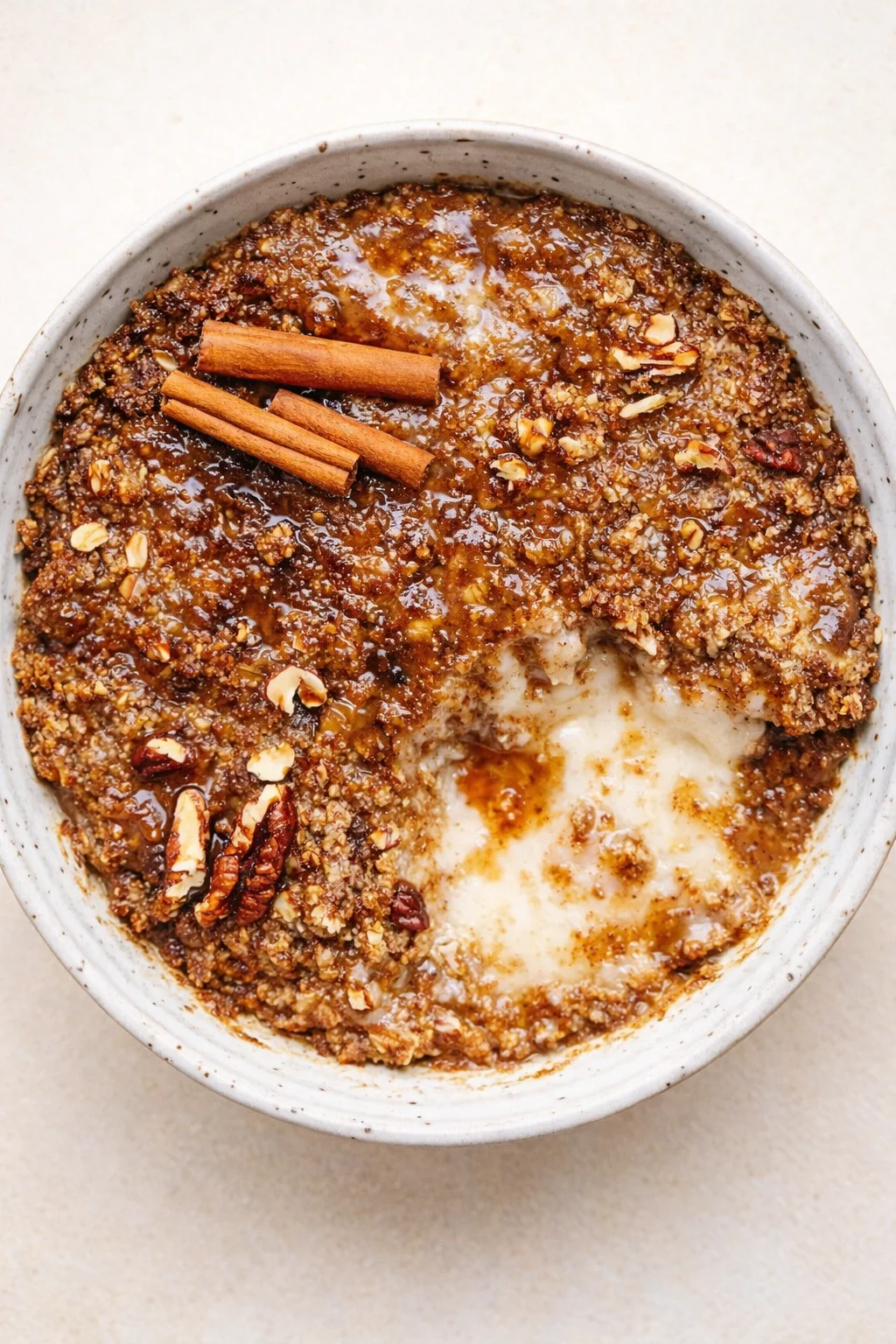 A rustic ceramic bowl holds cinnamon-pecan crumble with melted vanilla ice cream and cinnamon sticks on top.