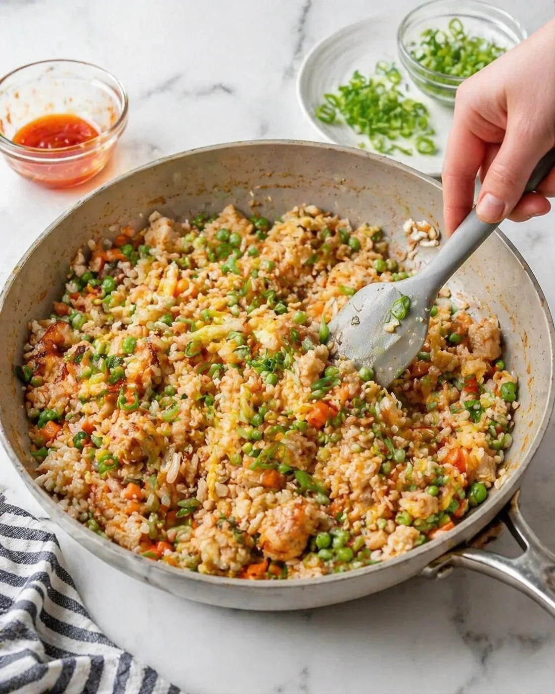 Fried rice with peas, carrots, and eggs in a skillet being stirred.