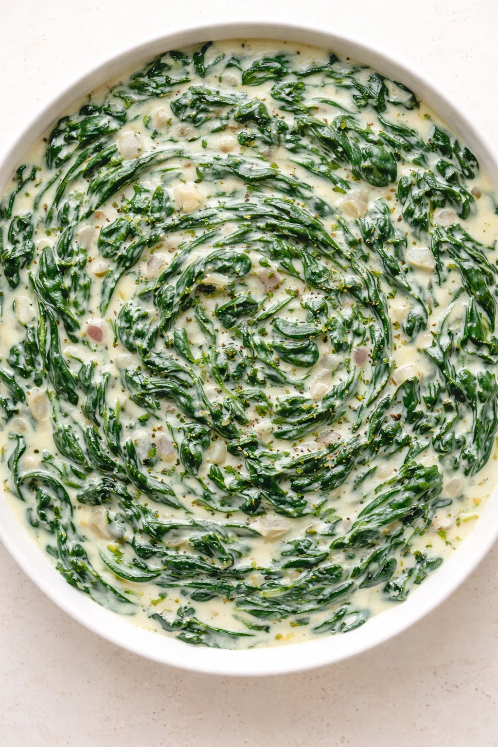 top-down view of a white bowl with creamed spinach and emerald-green ribbons swirled