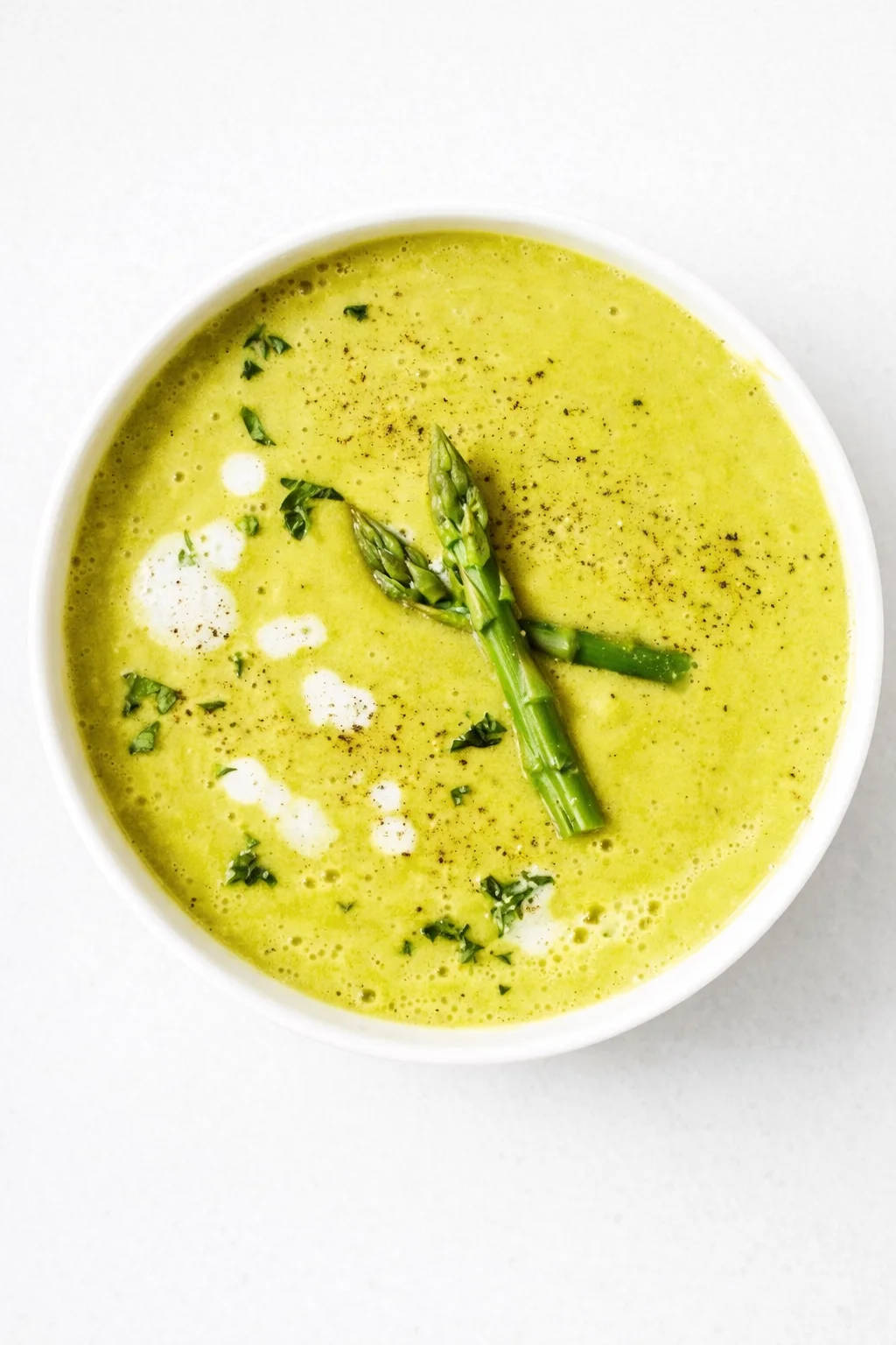 Creamy green asparagus soup in a white bowl, garnished with asparagus spears and herbs.